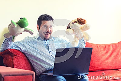 Happy father sitting on sofa communicating trough video call on laptop with his children showing them toys and presents Stock Photo